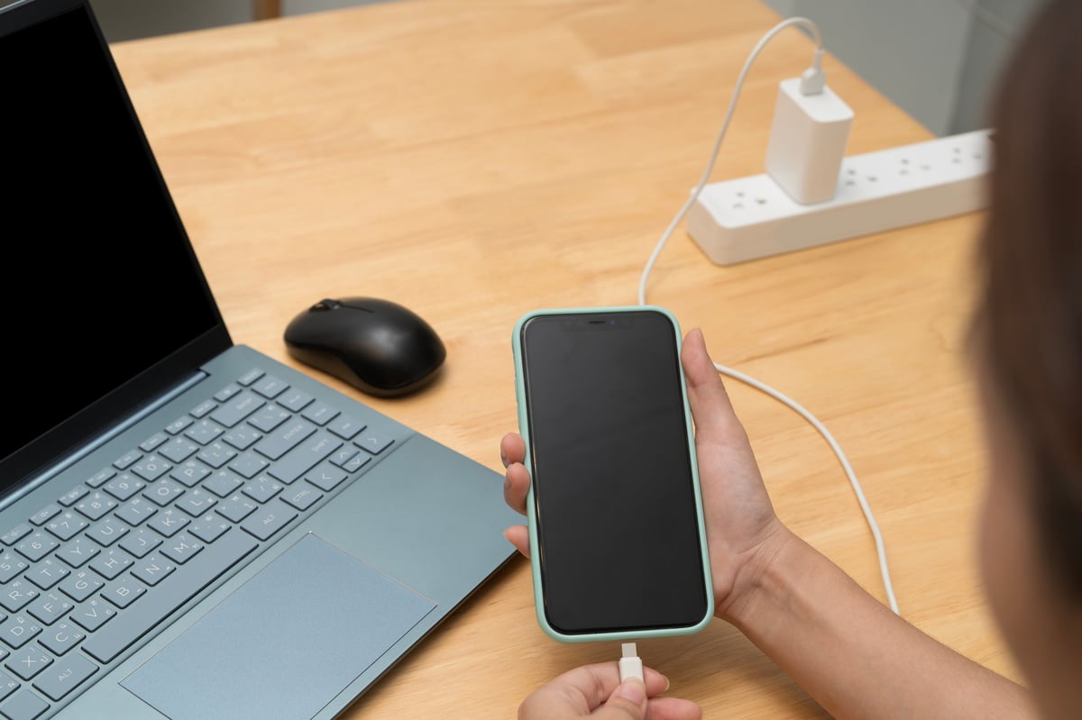 Person connecting a cable beside a laptop on a desk
