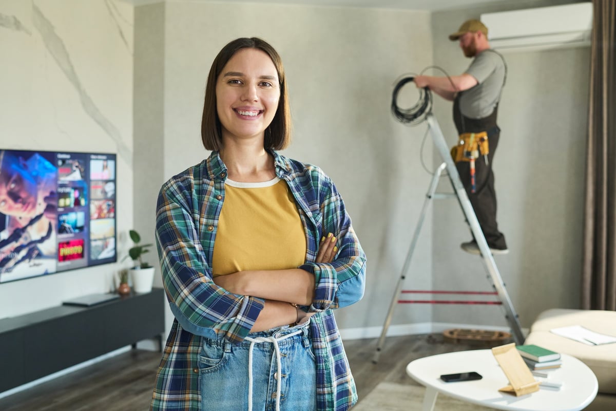 Homeowner smiling while a technician installs equipment in her living room